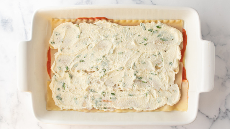lasagna noodles spread with cheese in a white baking pan