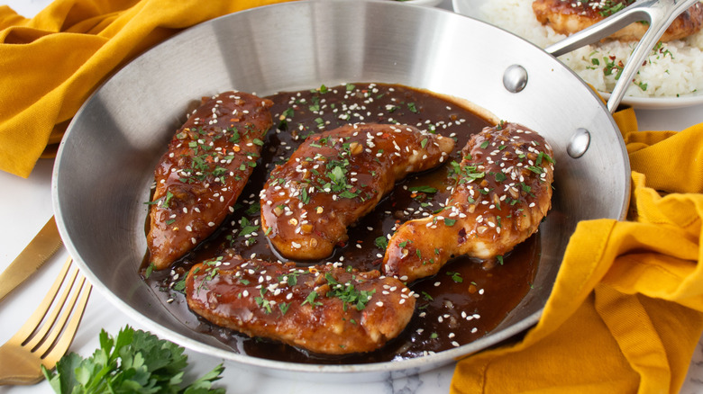 chicken tenders in brown sauce with sesame seeds in a metal frying pan