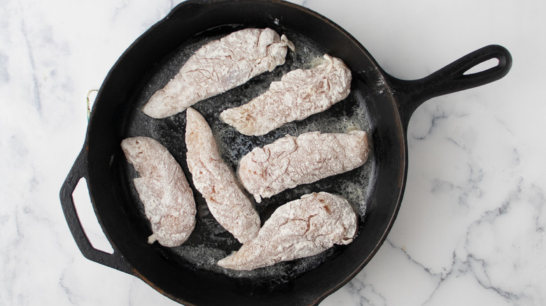 raw flour-coated chicken pieces in a black frying pan