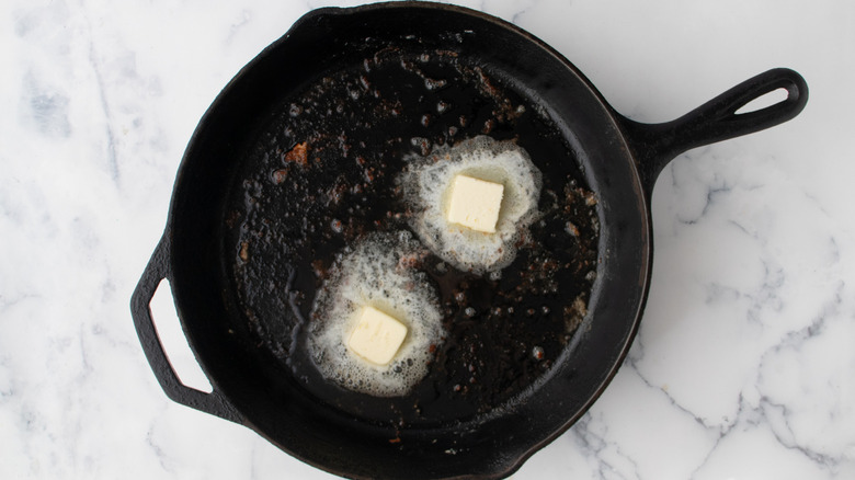 two butter chunks melting in a black frying pan