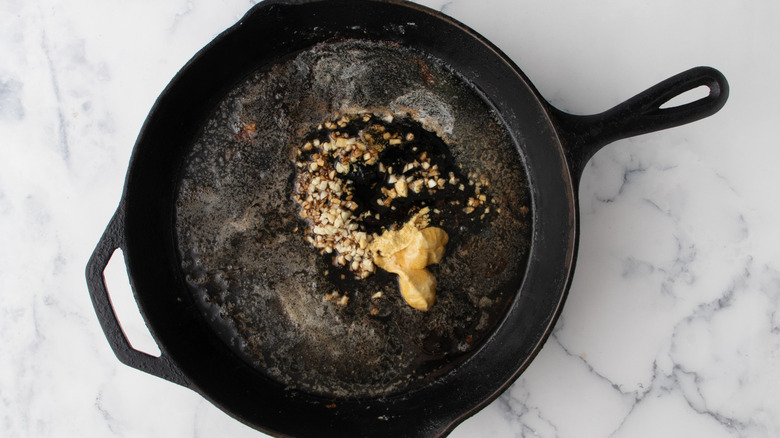liquid, chopped garlic, and mustard in a black frying pan