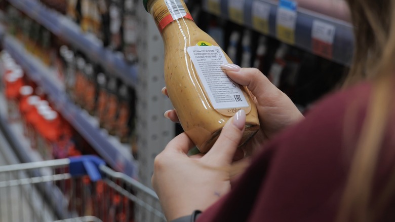 a woman reads the back of a salad dressing bottle