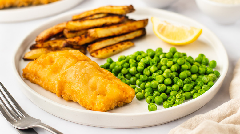 Plate of fish and chips with peas and lemon wedge