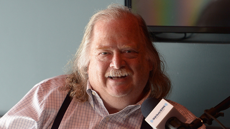 Food critic Jonathan Gold smiling in front of a microphone with a TV in the background