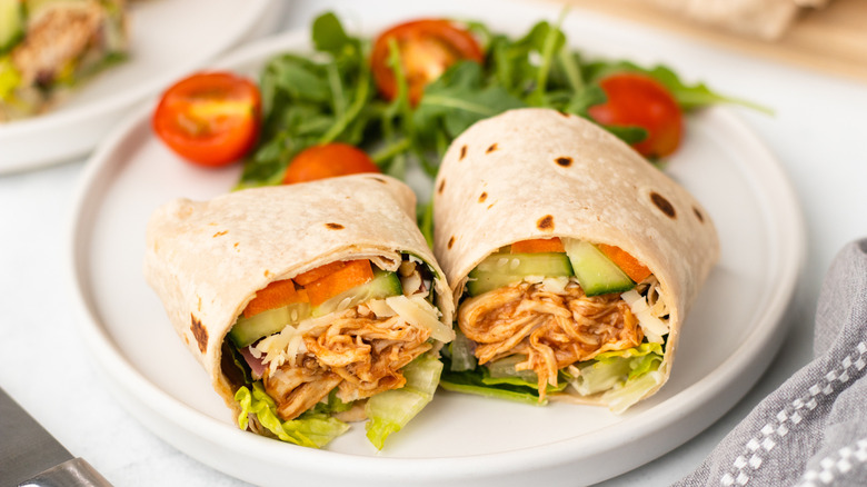 Halved BBQ chicken and crunchy veggie wrap on plate with side salad