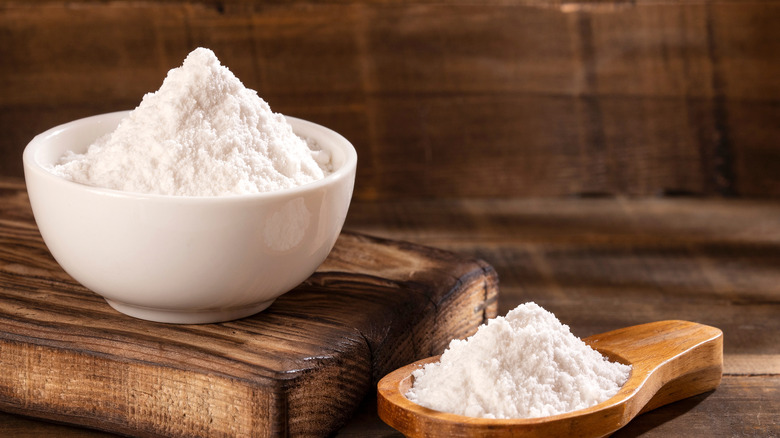 Baking soda in a white bowl and in a wooden spoon
